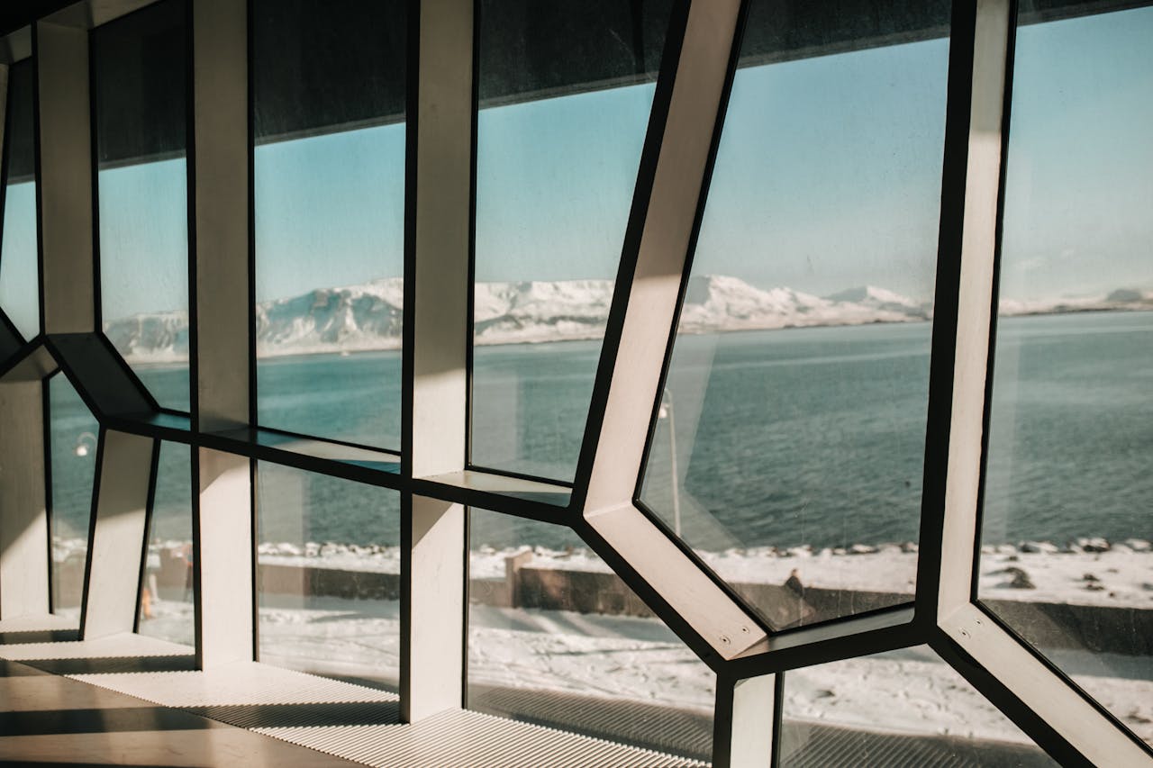 Geometric window design reveals snowy mountains and calm sea view, blending modern architecture with nature.
