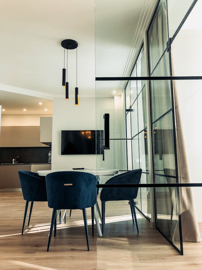 White table and dark armchairs placed near glass wall in contemporary spacious apartment with open plan kitchen in minimalistic style