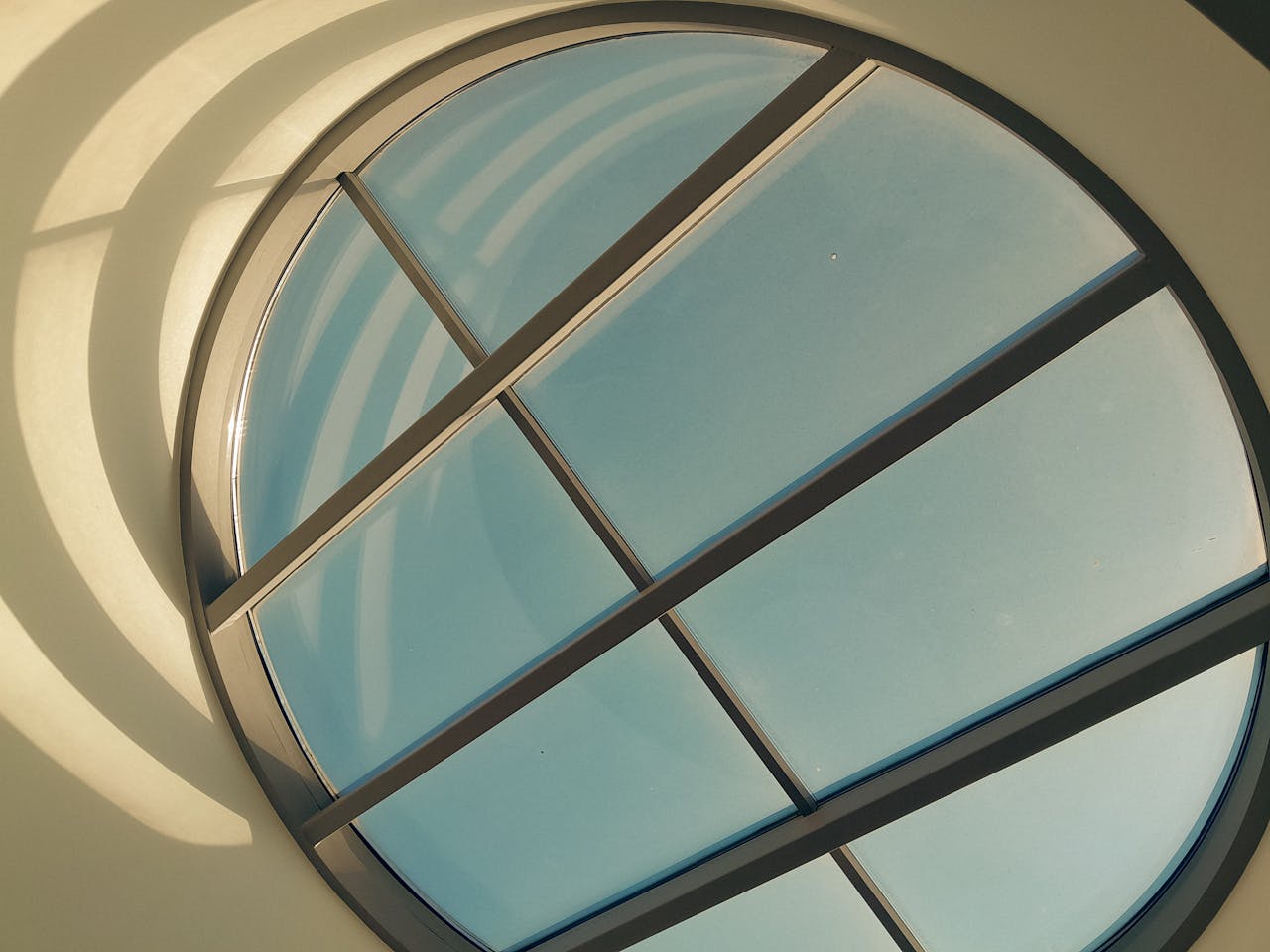 A modern circular skylight with artistic sunlight patterns casting shadows on the wall.